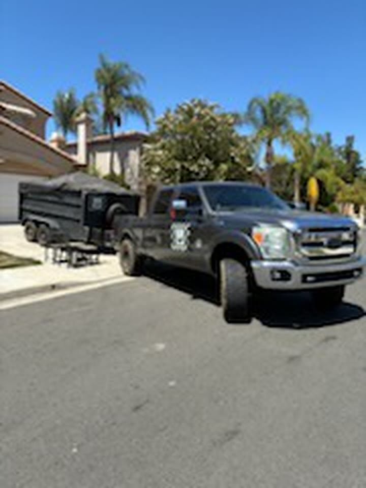 Junk removal truck towing a loaded dump trailer down a residential street