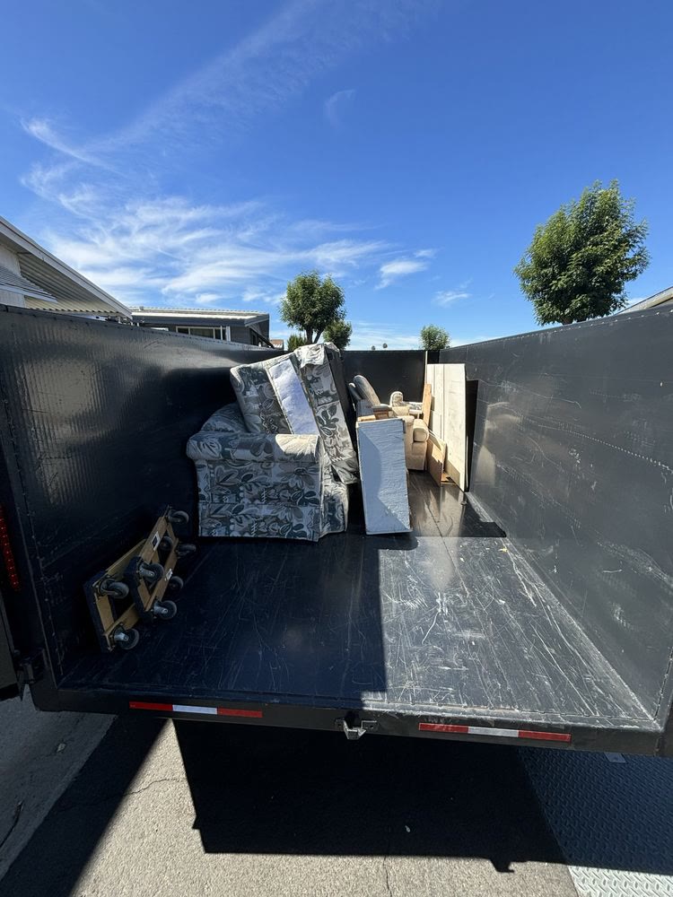 Dump trailer loaded with a sofa, cushions and household furniture outside a home